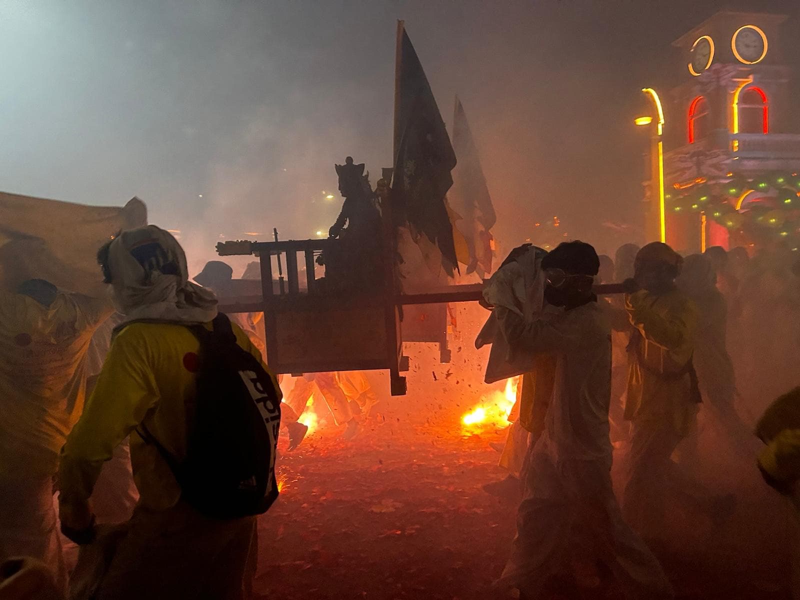 Photo of four Buddhists carrying a shrine over their shoulders in the middle of the sparks at the Vegetarian Festival, in Phuket, Thailand. Foto de quatro budistas carregando um santuário sobre os ombros no meio das faíscas no Festival Vegetariano, em Phuket, Tailândia.