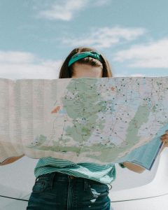 Photo by Leah Newhouse: https://www.pexels.com/photo/woman-looking-at-the-map-3935702/

The image shows a lady covering her face and good part of her body, looking closely to a map, whilst sitting on her car.