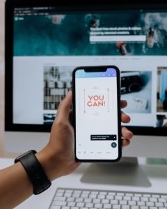 Photo by cottonbro studio: https://www.pexels.com/photo/holding-a-smartphone-in-front-of-an-imac-5082580/. This photo, featuring a hand holding a phone displaying the message “you can” in front of a desktop computer, exemplifies my list of apps for solo female travel in 2025.