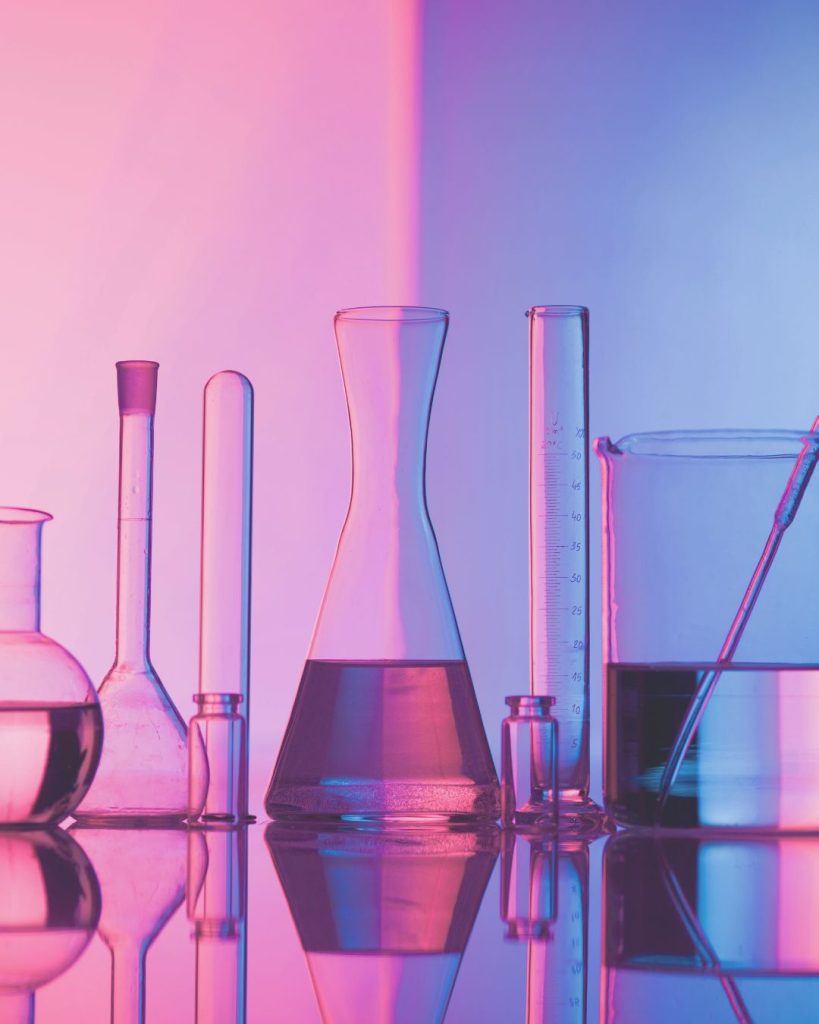 Foto em tons de roxo e rosa, com sete frascos de laboratório.
