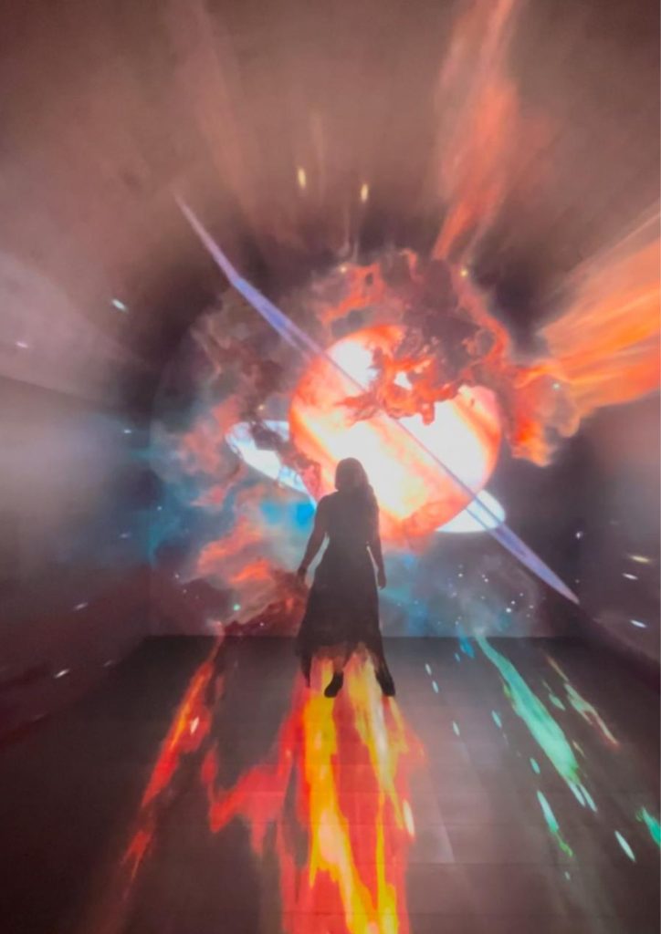 spirituality-from-woo-woo-to-something-that-changed-my-life A photo of me wearing a black floral skirt, a black sleeveless top, and black sneakers, standing in a hologram of the Universe at the Space and Cube Museum in Bangkok.