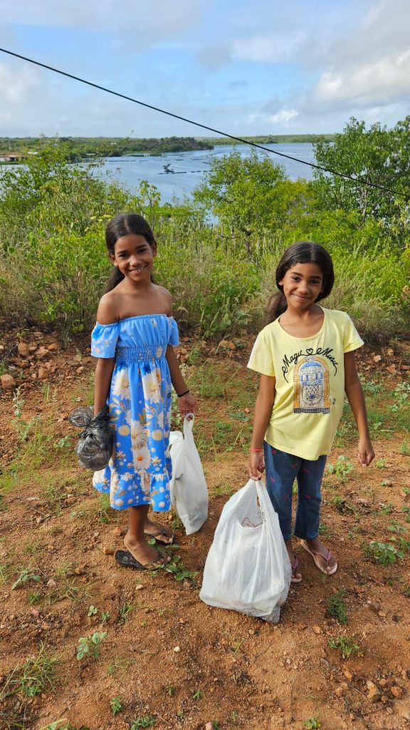 Imagem de duas meninas indígenas, do povo Pankararu Opará. As duas meninas possuem cabelos longos e escuros, amarrados em um rabo-de-cavalo. A menina da direita usa um vestido azul florido, enquanto a da direita, usa uma camiseta amarela.